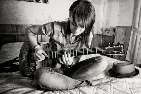 woman playing acoustic guitar on her bed
