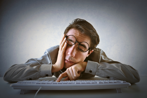 exhausted man hunched over computer keyboard from Shutterstock.com